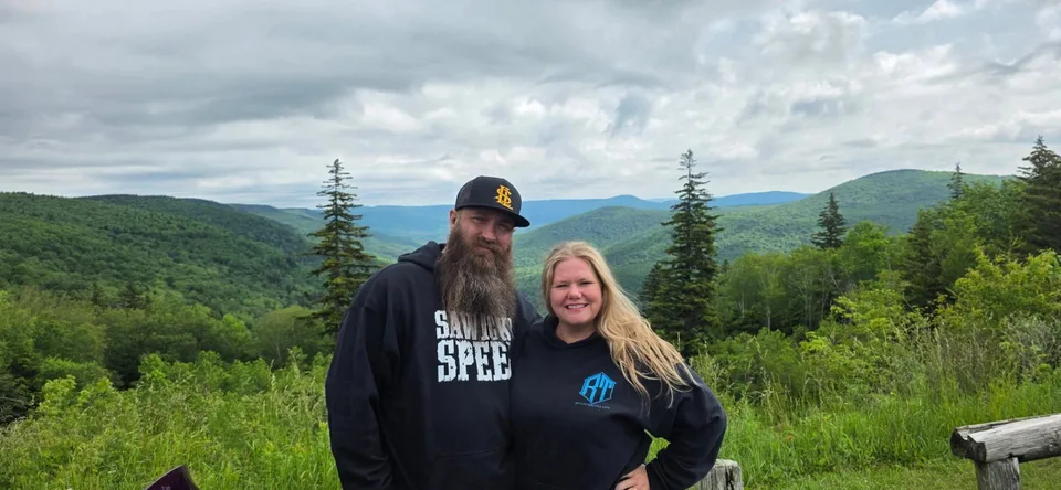 Two riders at an overlook with forested mountains stretching behind them
